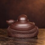 Rear view of the dark brown purple clay Laughing Buddha showing smooth shoulders and textured robe