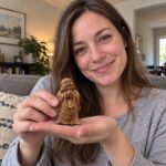 A woman holding the 8 cm cypress wood Laughing Buddha naturally on her palm in room light