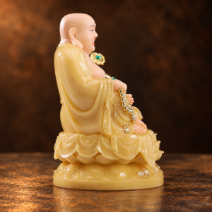 Side studio view of the painted composite Laughing Buddha in a yellow robe on a lotus base
